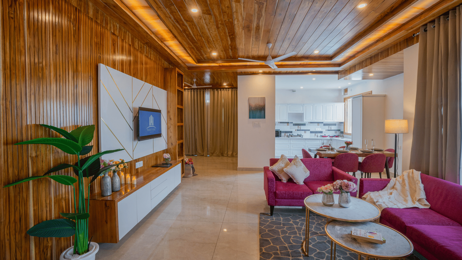 A living area at Perfectstayz Value Paradise, Mussoorie, with wooden walls, a television, a potted plant, a sofa set, 2 coffee tables, and ceiling lights.