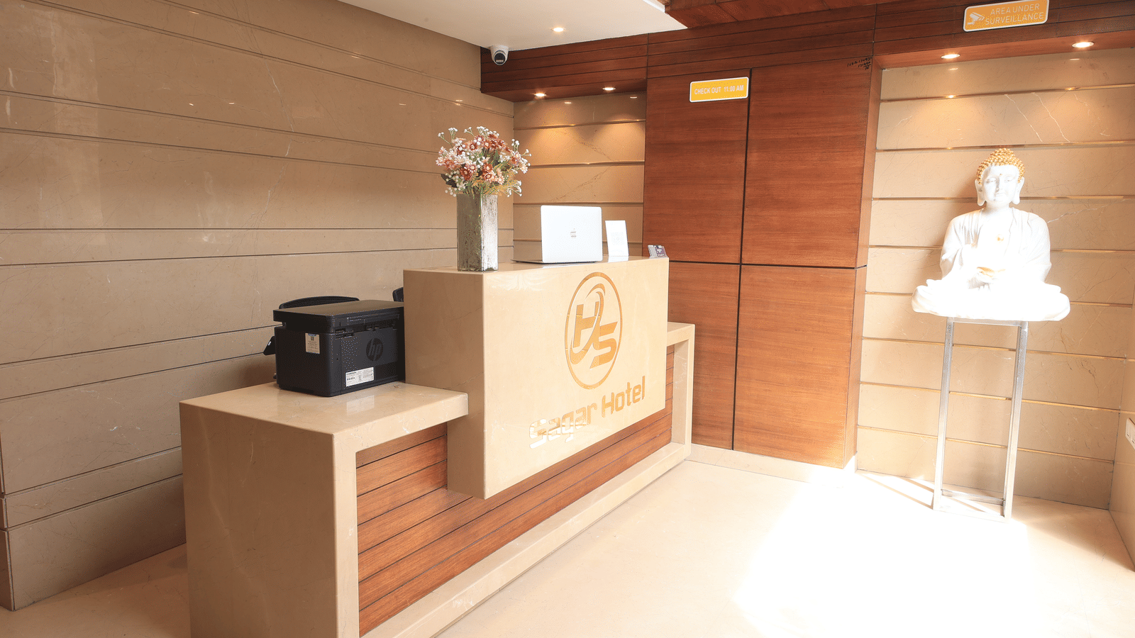 A hotel reception area, featuring a reception desk with a logo, a printer, and a statue on a stand | Perfectstayz Value Sagar