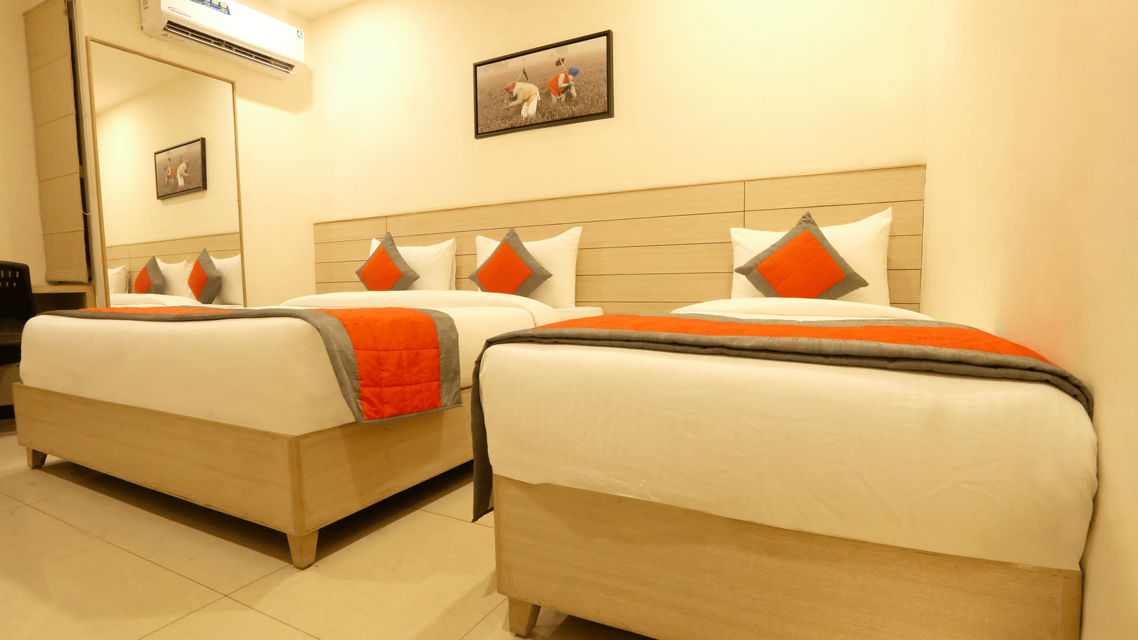 A hotel room, featuring 2 single beds side-by-side with white linens and orange accent runners and pillows, and a painting above the beds | Perfectstayz Value Sagar