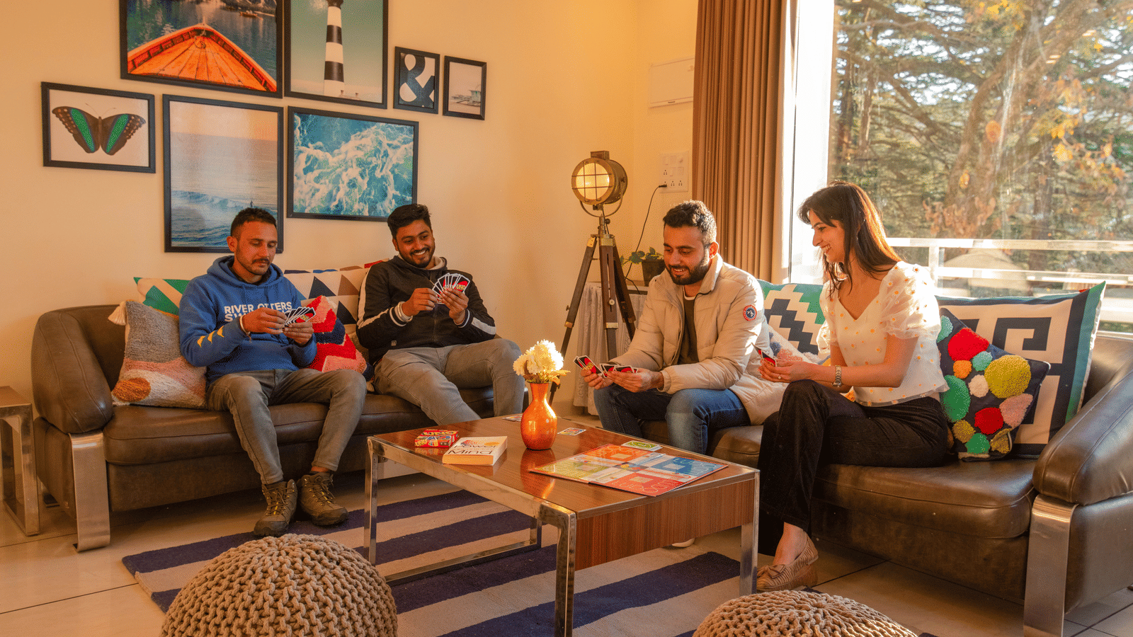 A group of people sitting in a living room with sofas, a table, wall art and large windows at Perfectstayz Value Shimla (Namah Retreat).