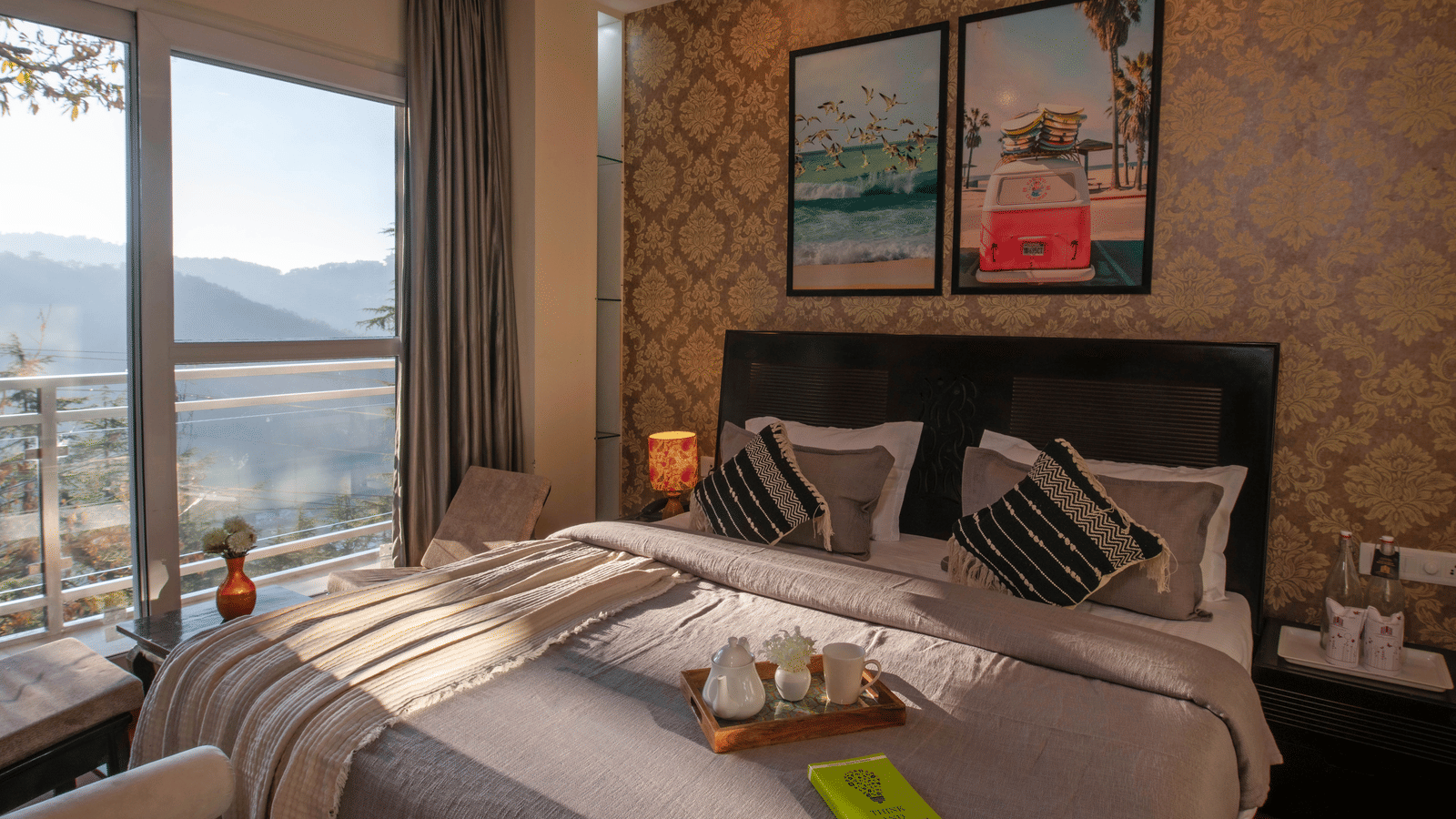 A bedroom at Perfectstayz Value Shimla (Namah Retreat) with a king size bed with a tray of cups and kettles, wall art, side lamps, and a window with hill views, 