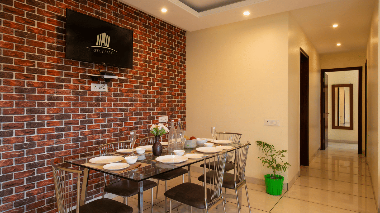 A dining area with a brick wall, a wall-mounted television, a dining table, and chairs at Perfectstayzz Value Shimla (Namah Retreat).