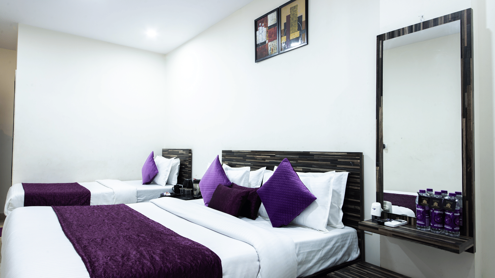 Hotel room with a double bed, twin beds, a mirror, and bottled water - Perfectstayz Value Umra Grace, Haridwar