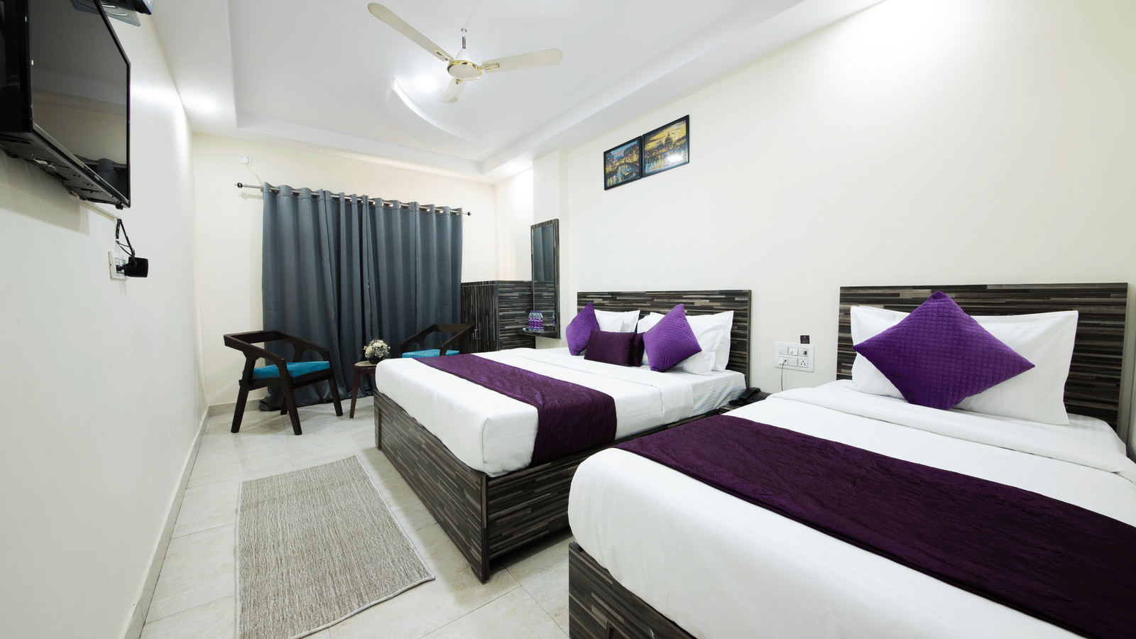 Double bed room with two beds, purple runners, a ceiling fan, seating area, and a TV - Perfectstayz Value Umra Grace, Haridwar