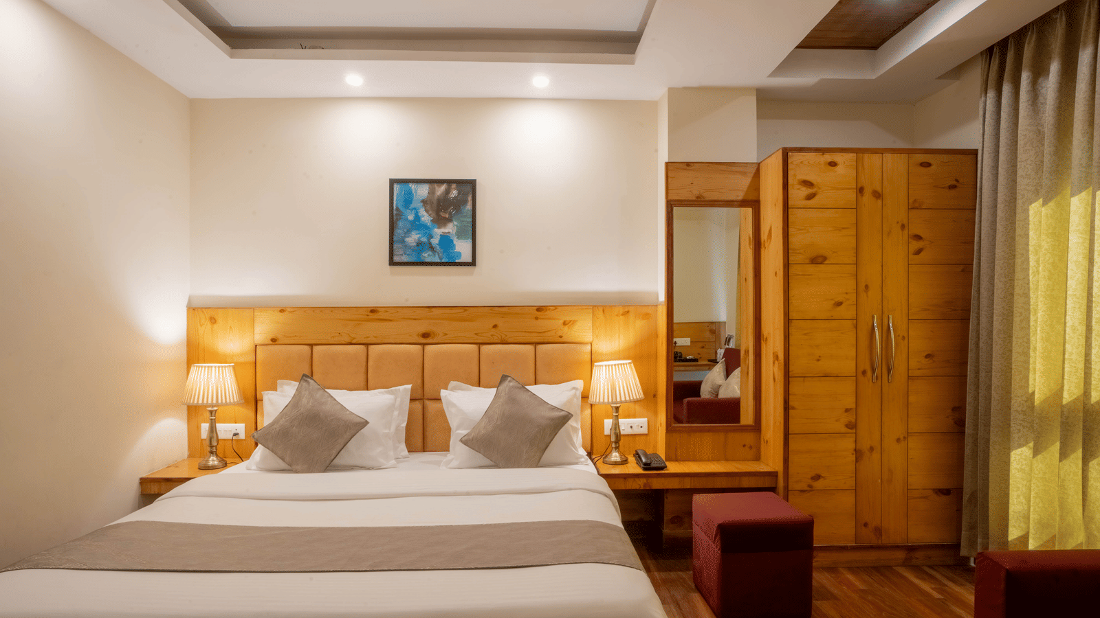 A hotel room, featuring a large bed with a wooden headboard, nightstands with lamps, a wooden wardrobe, and a small blue painting above the bed | Perfectstayz Value Valley Vista