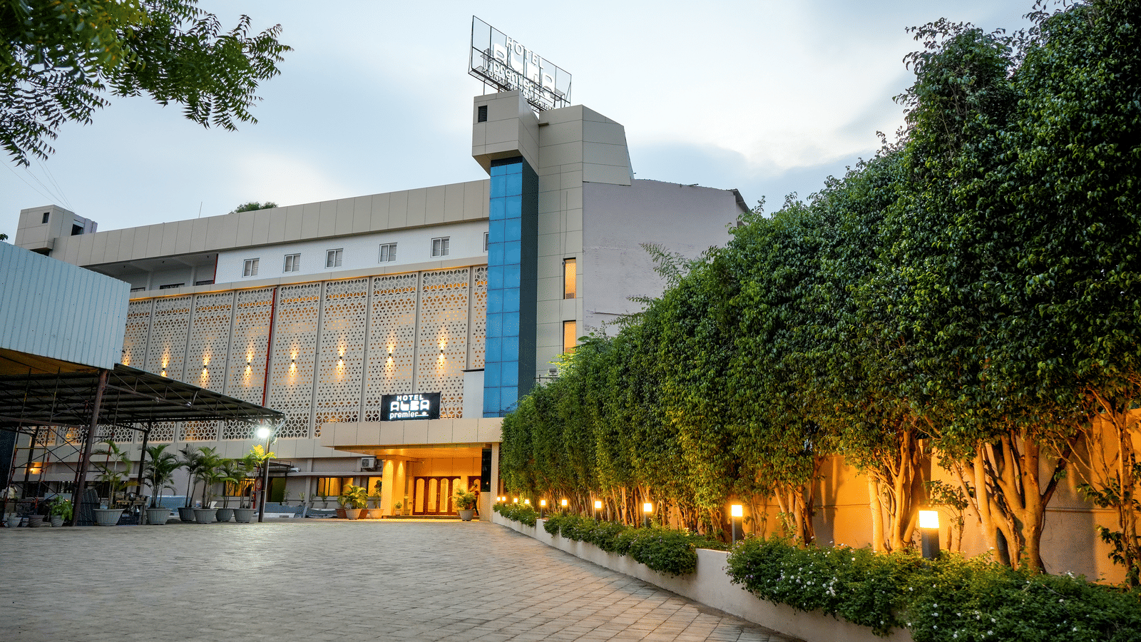 Exterior view of hotel building with driveway and trees at Pravasa Hotel, Kolhapur.