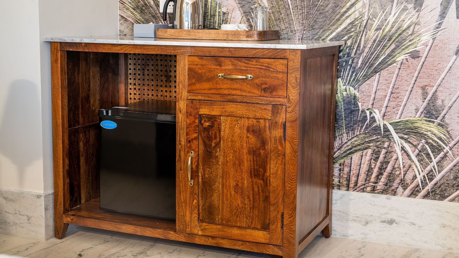 A shiny wooden cupboard with a modern safe in front of a wall with a tropical mural - Rajbagh Wellness, Udaipur