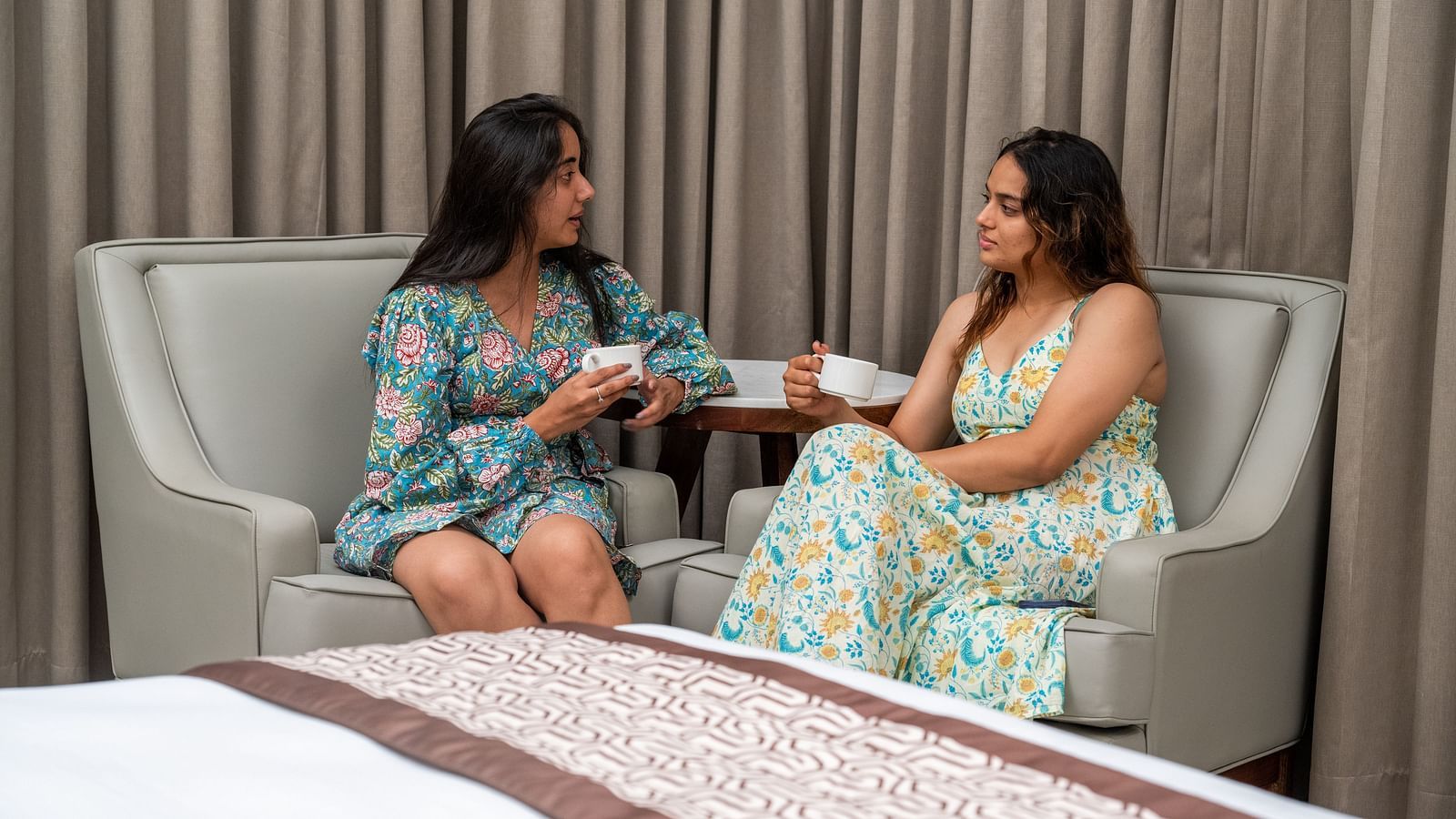 Two women holding coffee cups chatting with each other in one of our rooms - Rajbagh Wellness, Udaipur