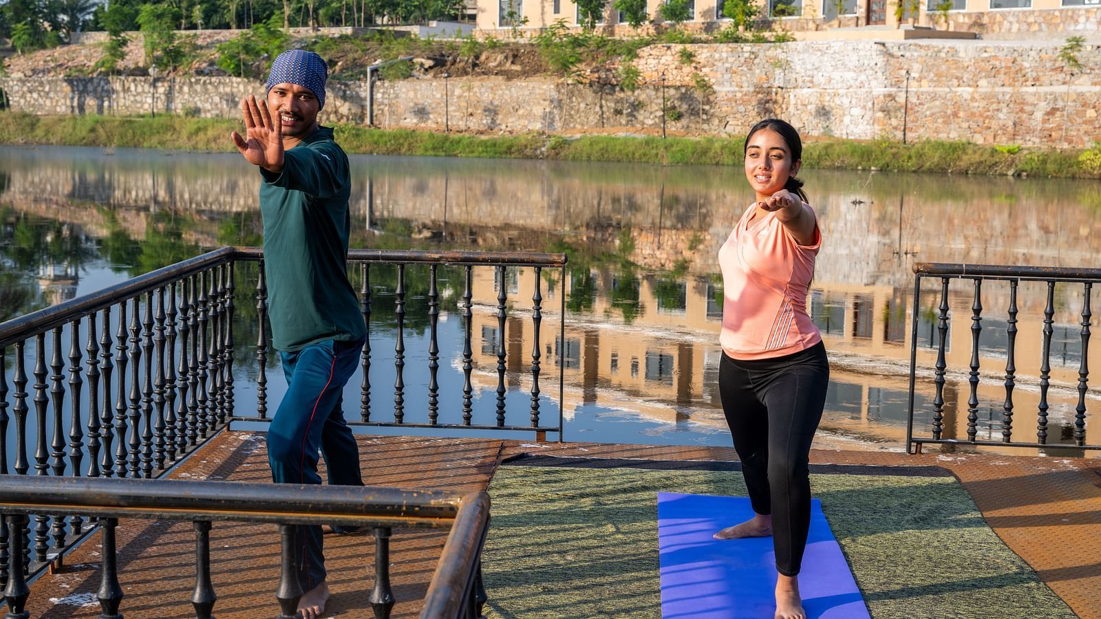 A woman being guided by our yoga instructor during a training session by a water body - Rajbagh Wellness, Udaipur.
