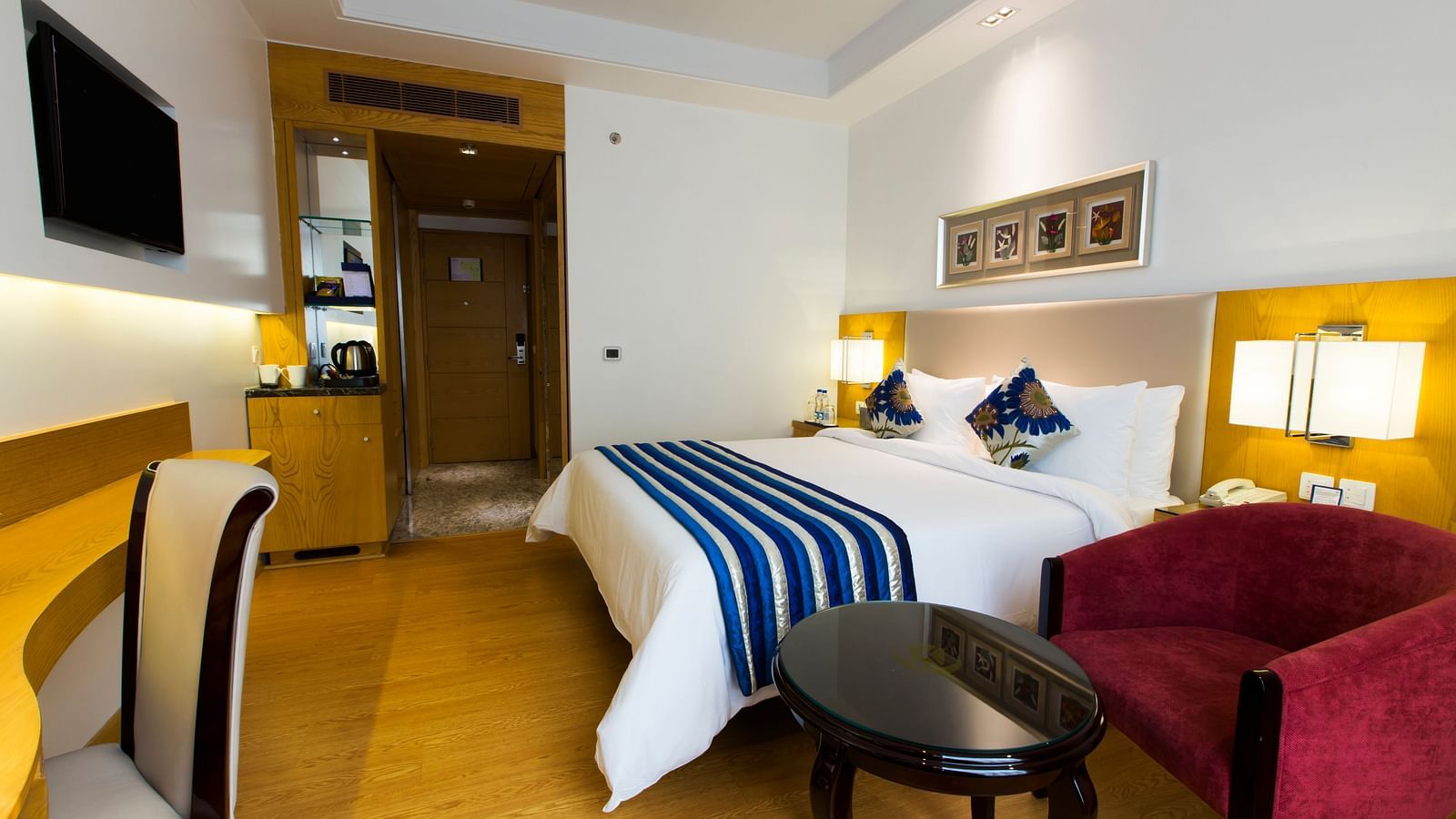 Corner view image of a bedroom featuring a double bed with a maroon coloured arm chain besides it - Ramada by Wyndham, Ghaziabad, Vasundhara