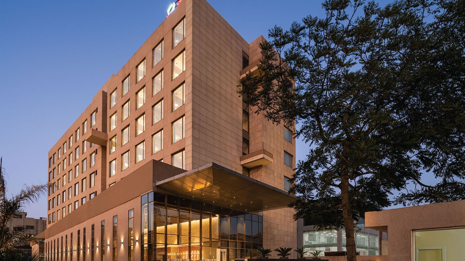 Ramada Encore by Wyndham, Bhiwadi | Hotel at night, warm lighting. Architecture emphasized, long lighted awning, silhouetted trees.