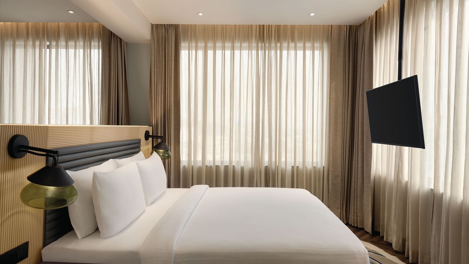 Ramada Encore by Wyndham, Bhiwadi |  Hotel bedroom with a white bed, TV, and large window with blinds.