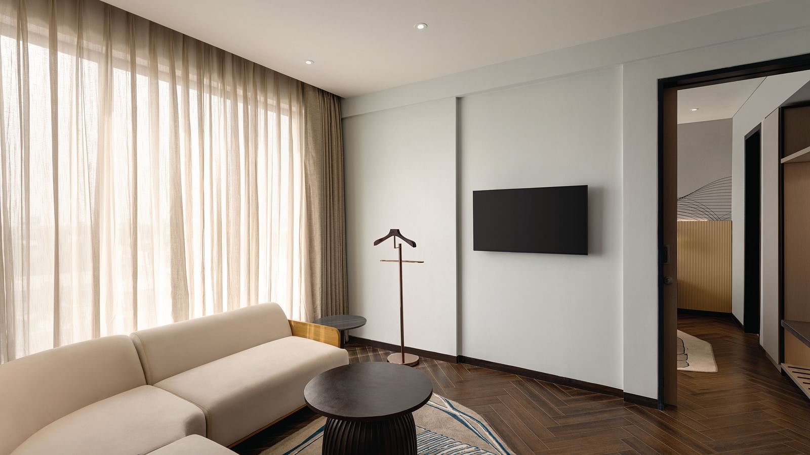 Ramada Encore by Wyndham, Bhiwadi |  Hotel suite with a living area, couch, TV, and a view into the bedroom.