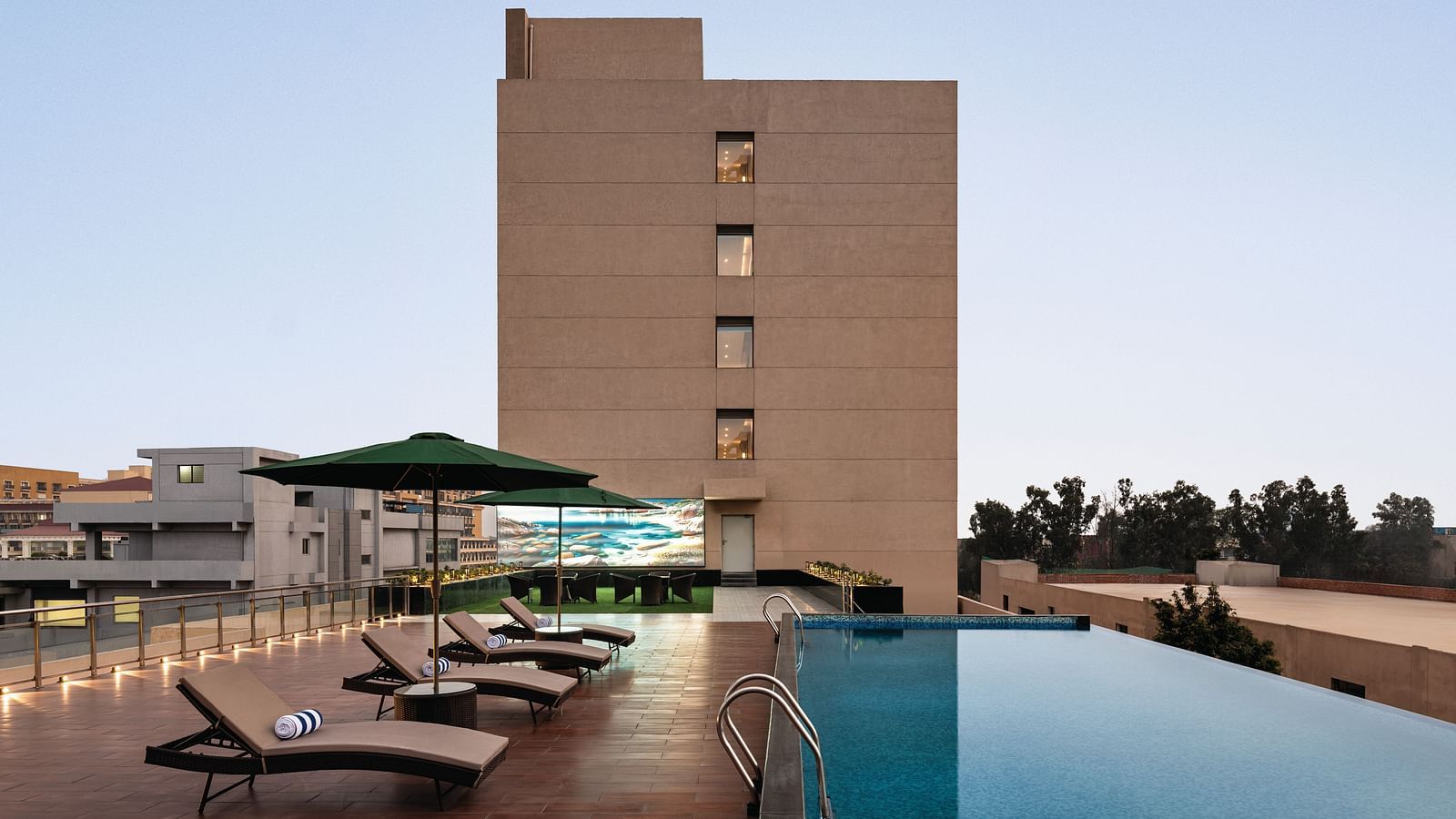Ramada Encore by Wyndham, Bhiwadi | Hotel exterior with a pool, lounge chairs, and a clear blue sky.
