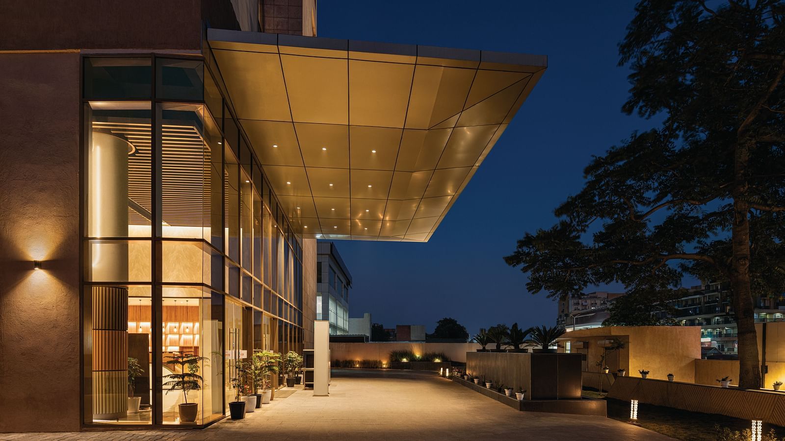 Ramada Encore by Wyndham, Bhiwadi |  Modern hotel exterior at night, brightly lit awning, large windows, paved walkway.