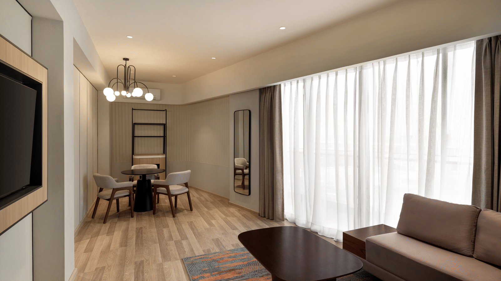 Spacious hotel suite living area at Ramada Encore by Wyndham Gurugram Dwarka Expressway, featuring comfortable seating, a television and natural light.