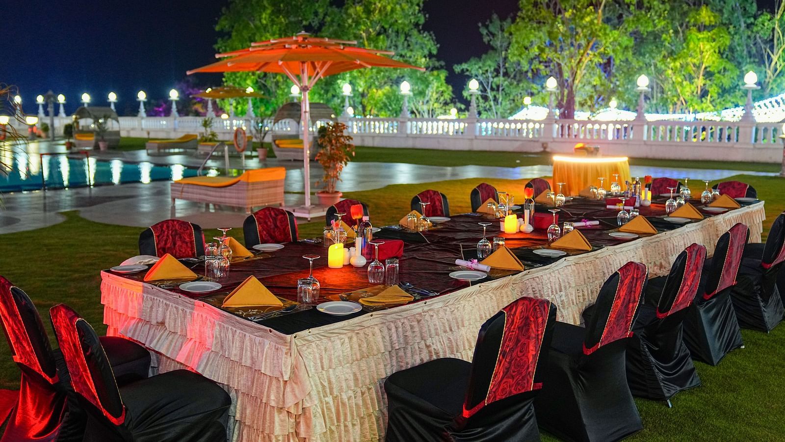 a set banquet table on a lawn with a swimming pool in the background at night - Ramoji Film City Hotels in Hyderabad 