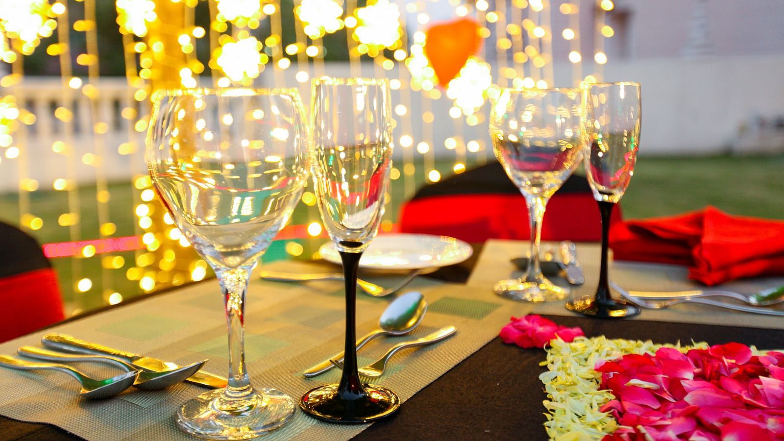 glasses set on a table with plates, cutlery and decoratations in the backdrop - Ramoji Film City Hotels in Hyderabad 