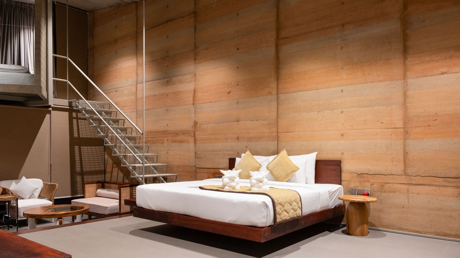 A room at RD's Nature Retreat, Bangalore featuring double size bed, a seating area with sofa sets and centre table, and flight of stairs leading to the next floor.