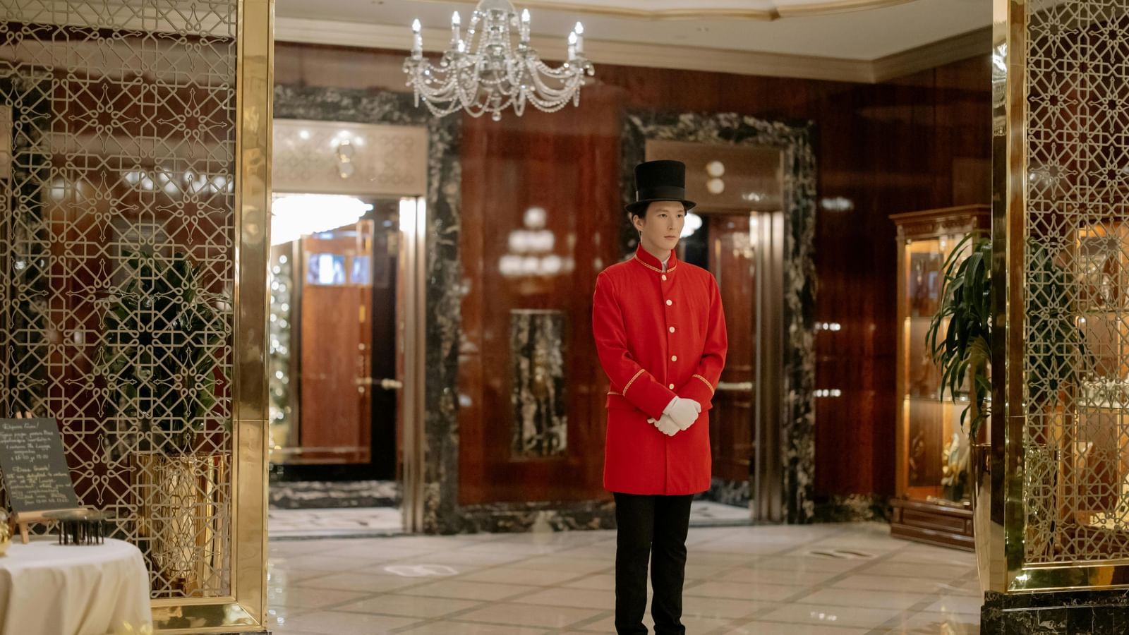 A hotel reception area with luxurious decor, marble floors, doors and a butler standing