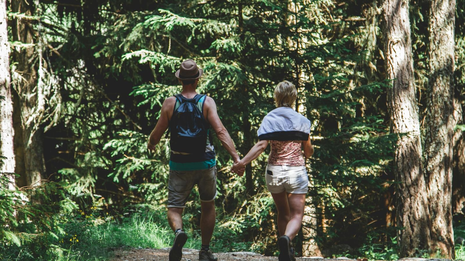 A man and a woman taking a walk among greenery filled with trees