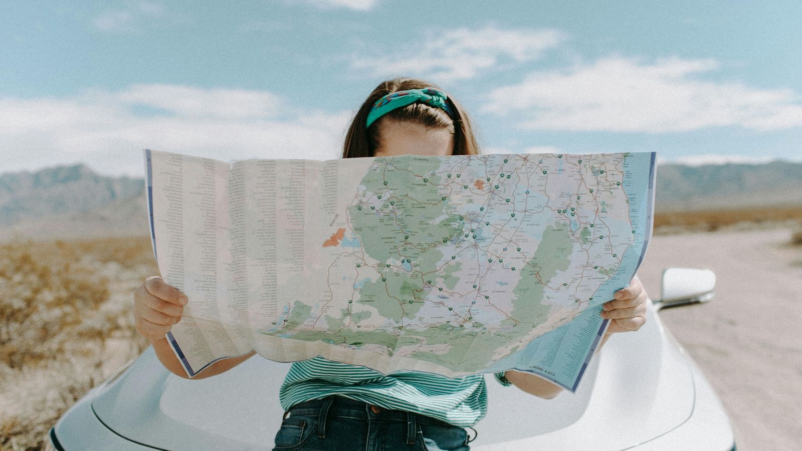 A woman looking at a map in front of a car alongside a road, with blue sky