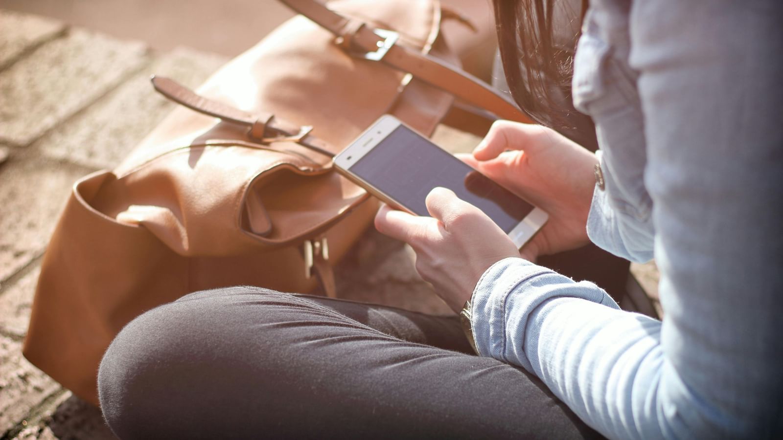 A woman with a phone in her hand and  bag near her