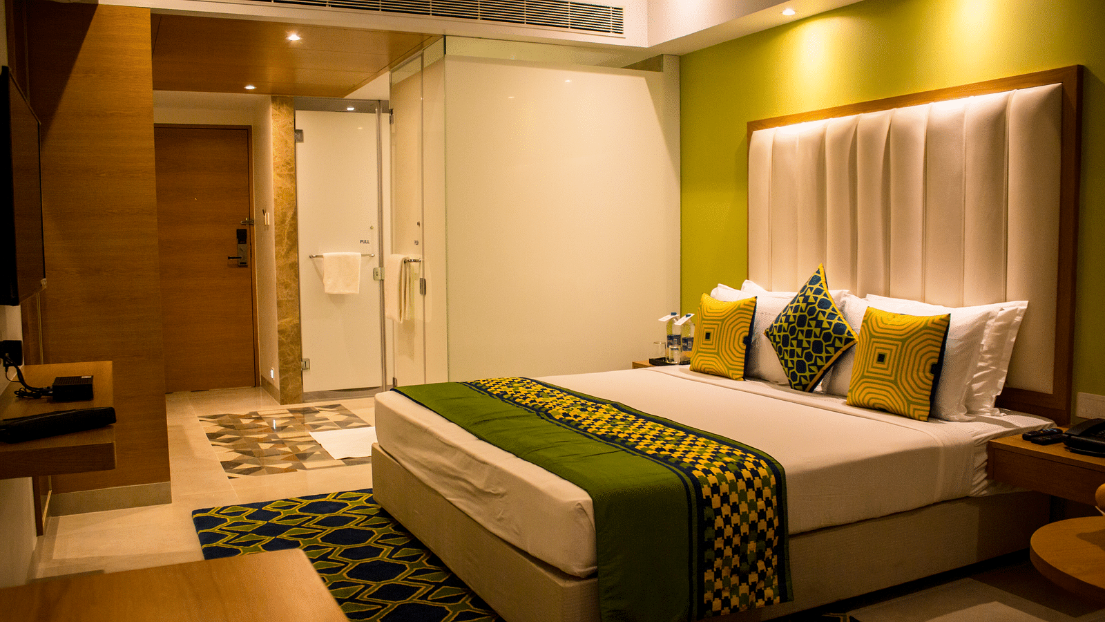 A room with a bed and  pillows arranged on it  along with  a side table | Regency Tirunelveli By GRT Hotels