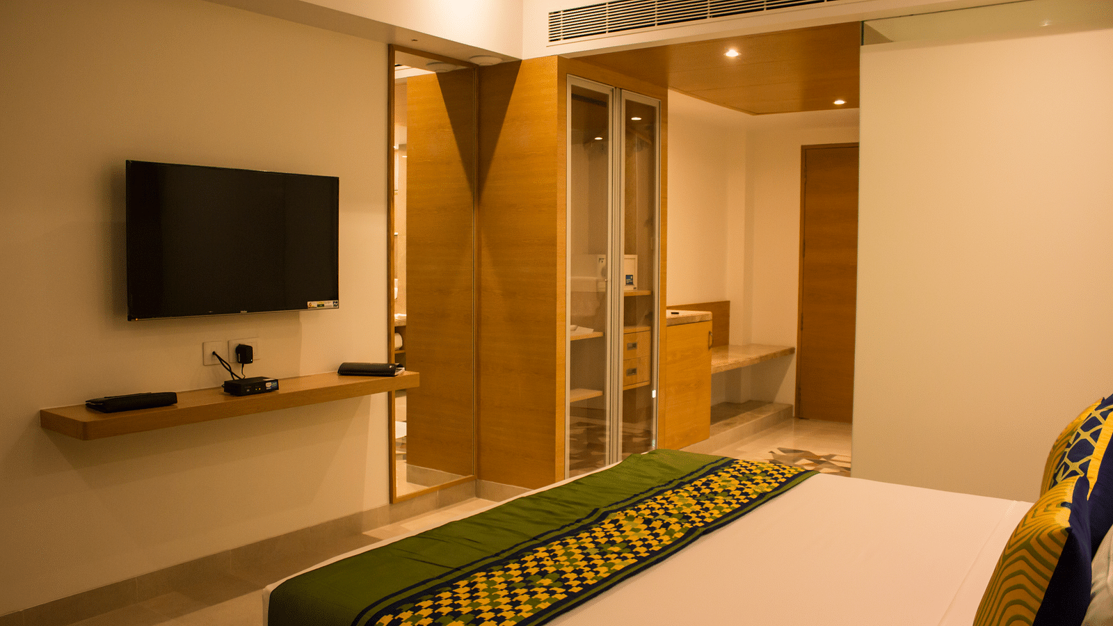 Side view of a room with a bed and  pillows arranged on it  along with  a TV | Regency Tirunelveli By GRT Hotels