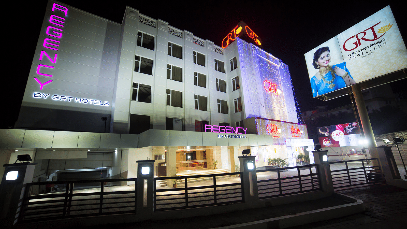 Regency GRT Hotels sign with purple letters and blue lights at night.