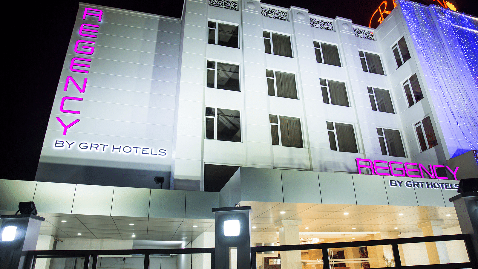 Regency GRT Hotels sign with purple letters and blue lights at night.