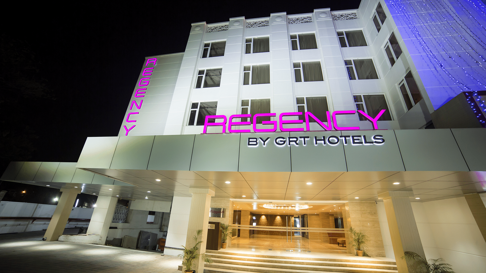 Regency GRT Hotels sign with purple letters and blue lights at night.