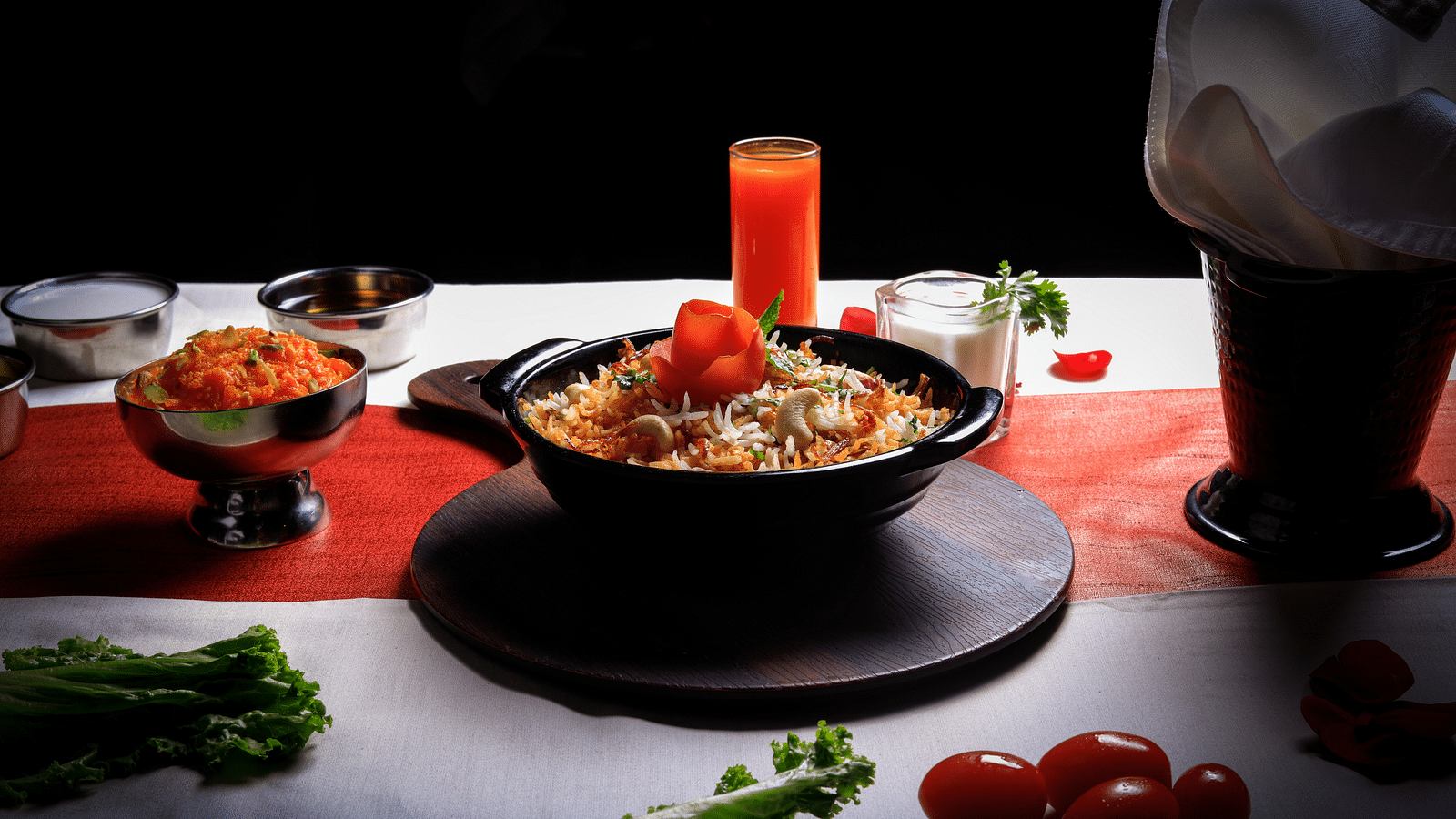  A bowl of creamy, orange-hued pasta topped with a dollop of red sauce and a sprig of parsley. The dish is accompanied by a glass of orange juice, a chef's hat, and various vegetables.