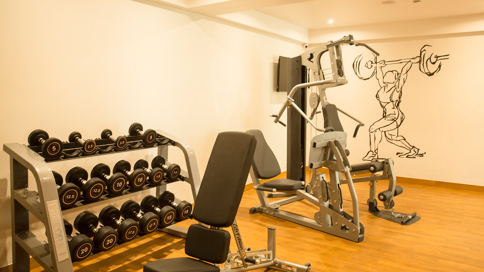Hotel gym with dumbbells, weight bench, and exercise machines | Regency Tirunelveli By GRT Hotels. 