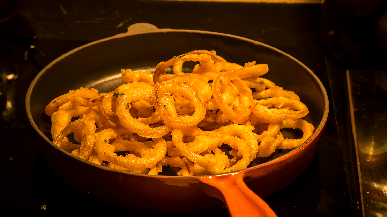 Golden-brown onion rings frying in a red pan.
