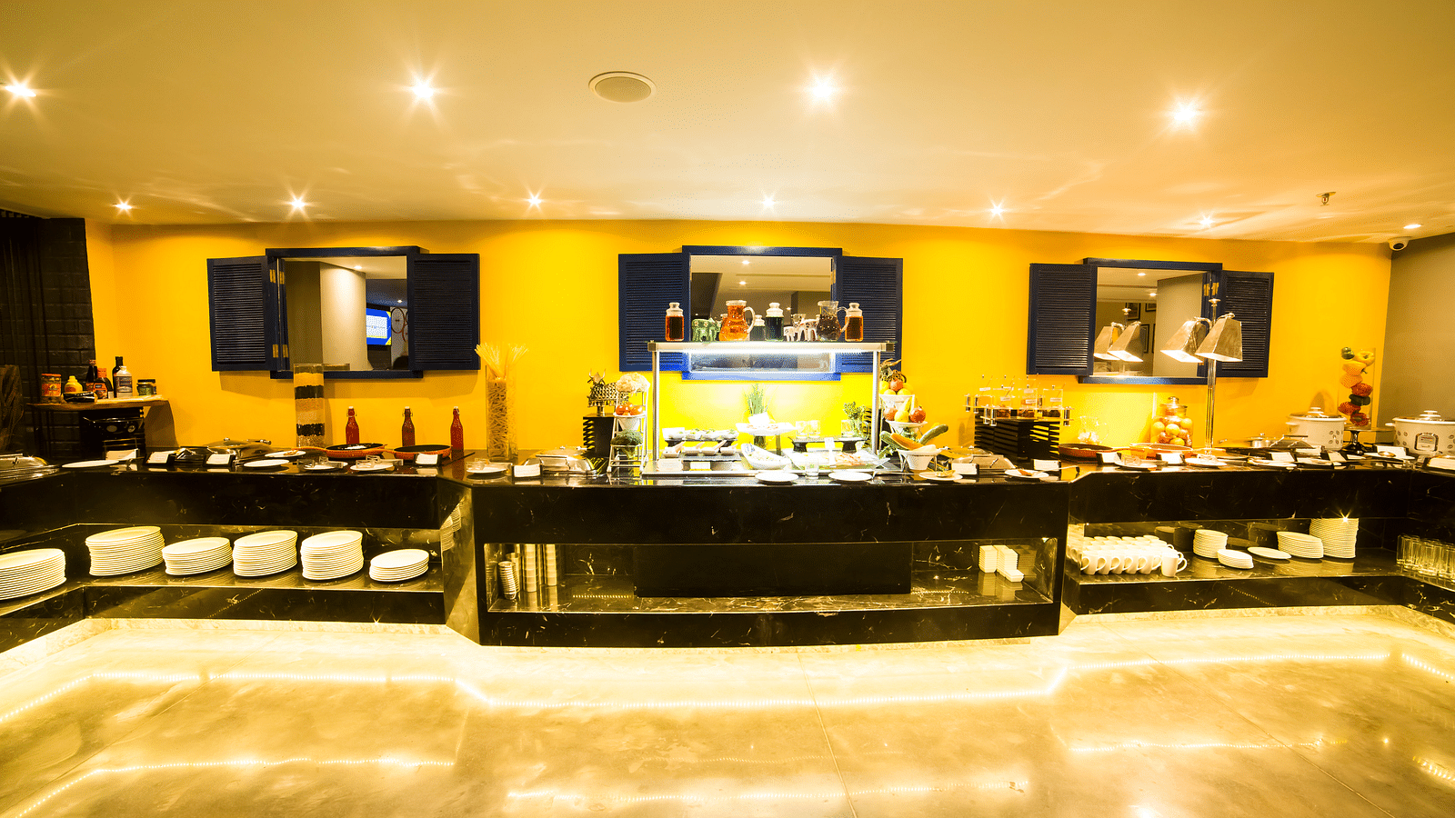Hotel restaurant with a buffet setup featuring a long counter with various food displays and yellow walls | Regency Tirunelveli By GRT Hotels 