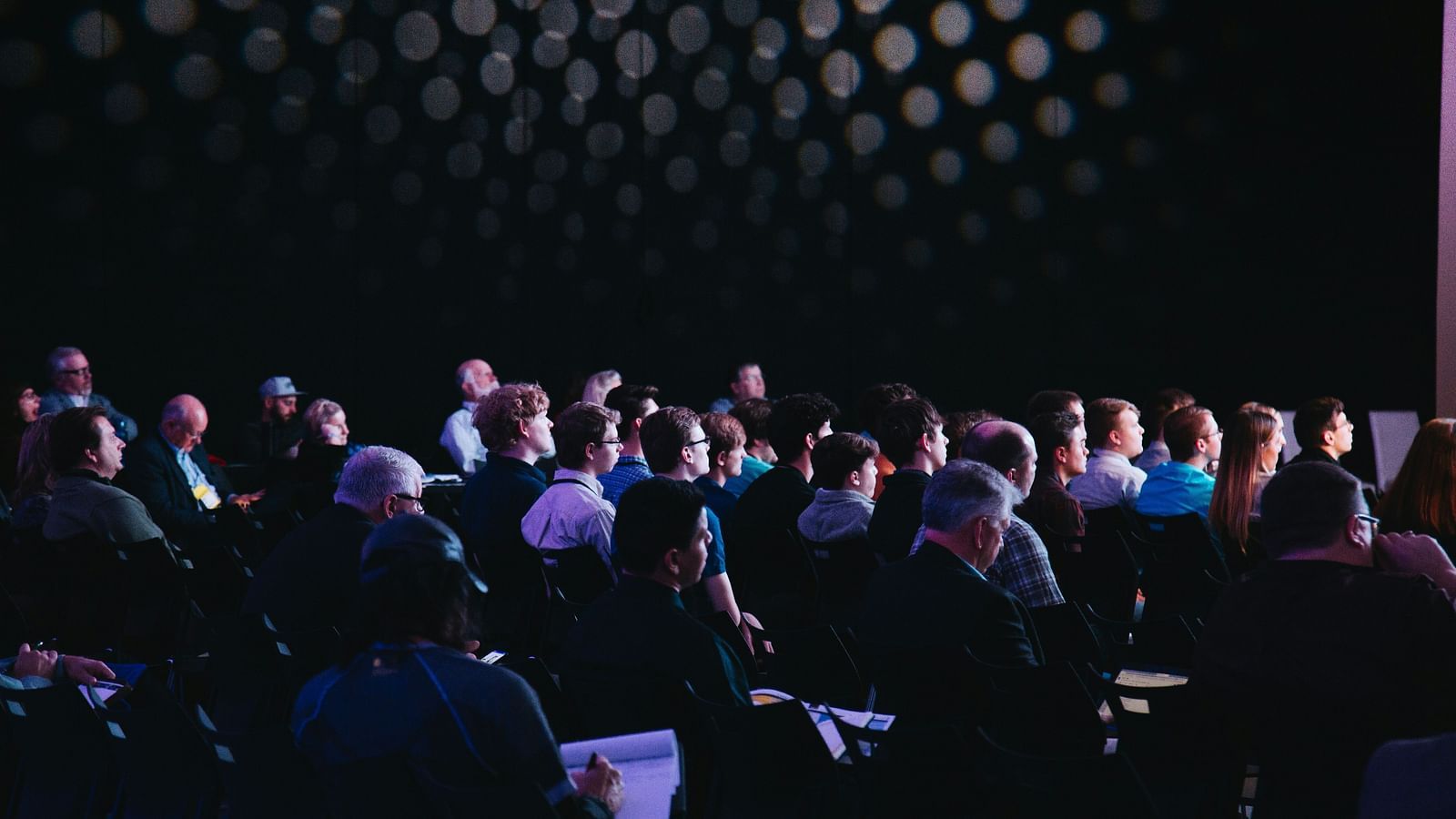 An overview of a conference with many people sitting and listening to a person on stage.