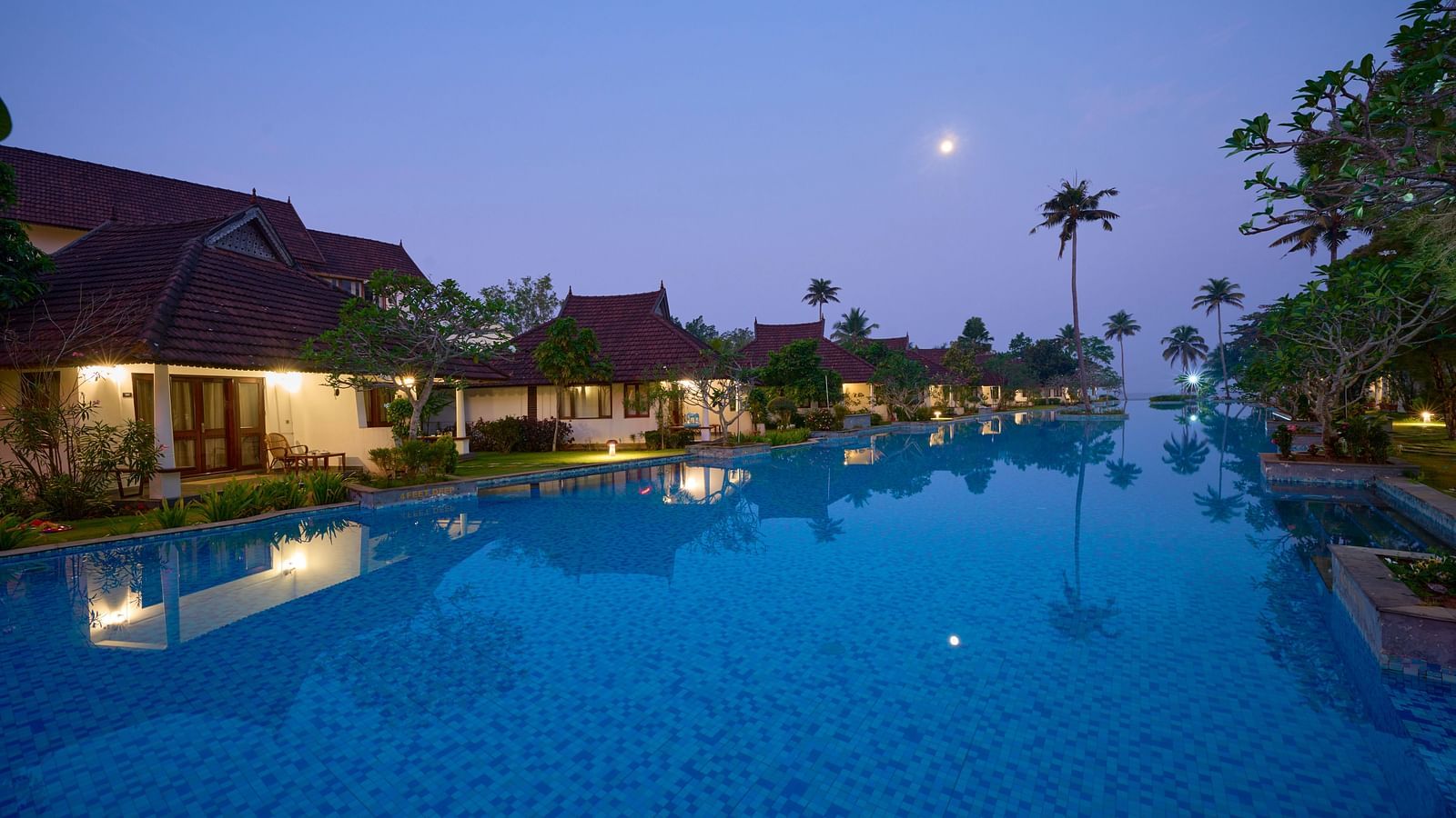 A view of the swimming pool with rooms and trees on the side - Rhythm Kumarakom.