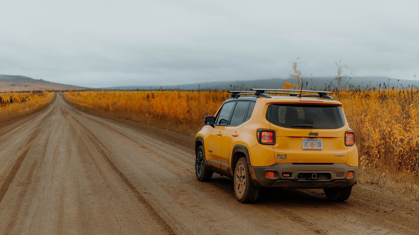 an image of solitary car travelling on a straight road with dried grass on either side.
