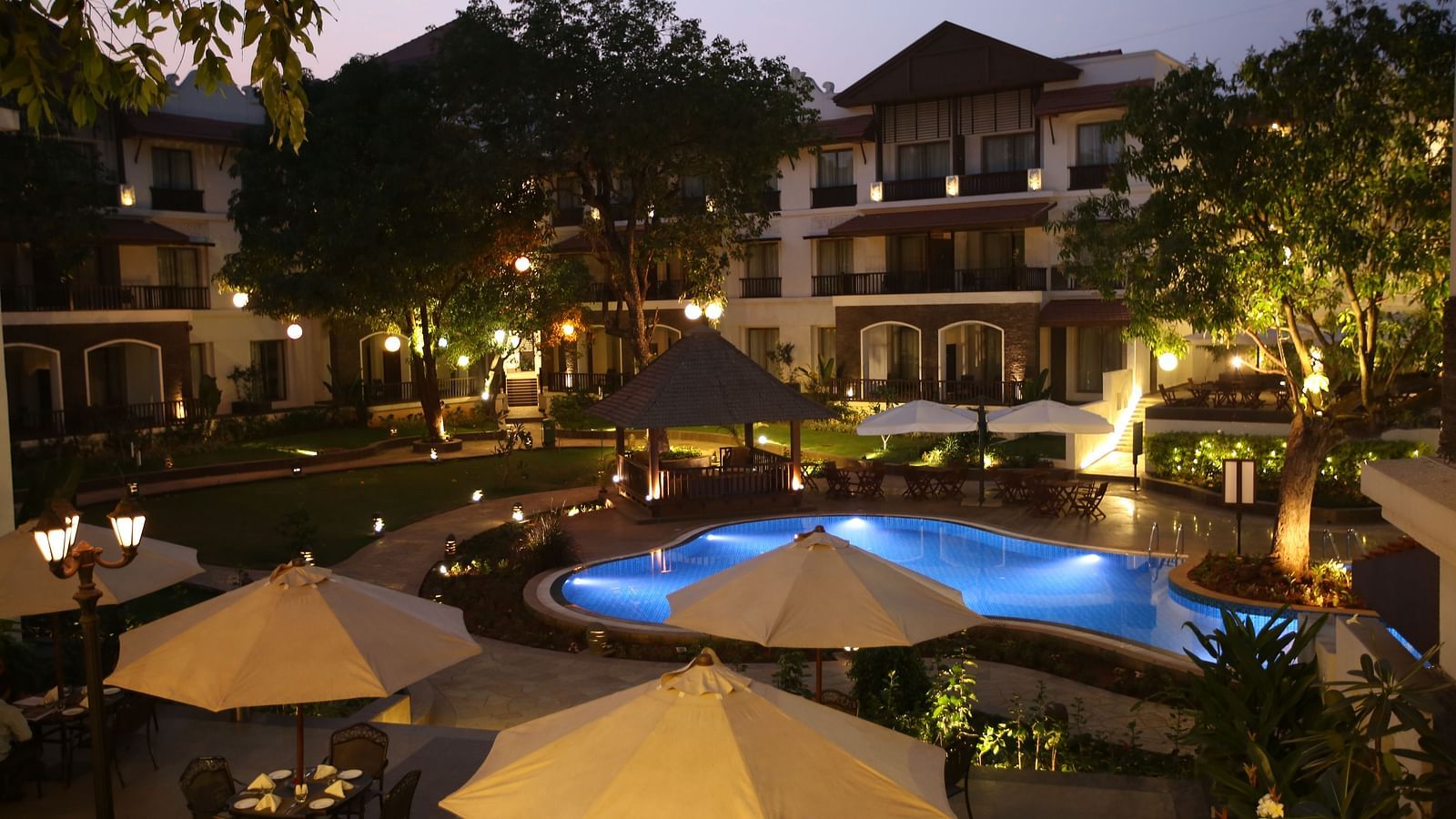 Seating arrangement of Courtyard Bistro with swimming pool lit up at night - Rhythm Lonavala