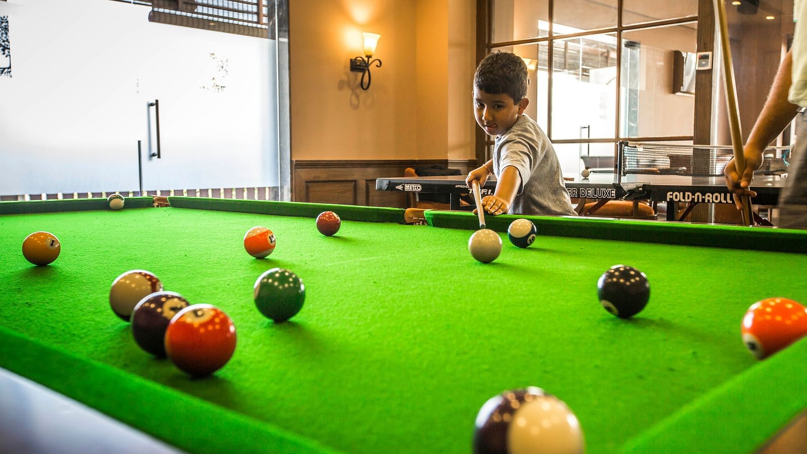 A child playing a game of pool with a glass partition behind him at the fun zone inside Rhythm Lonalava