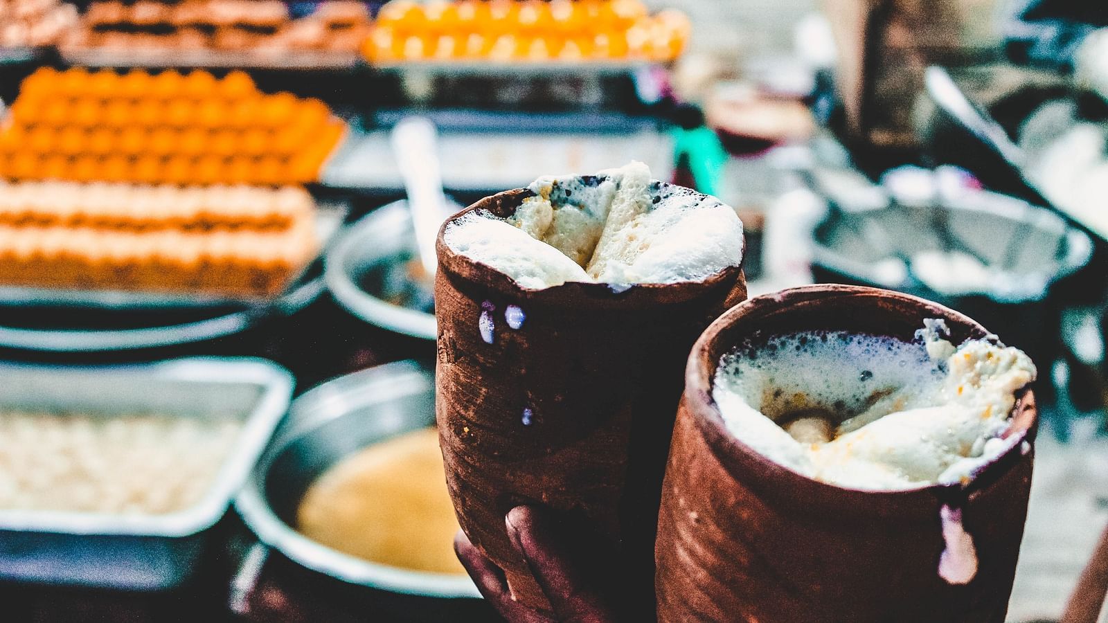 two tumblers full of lassi with laddos and other sweet dishes in the background