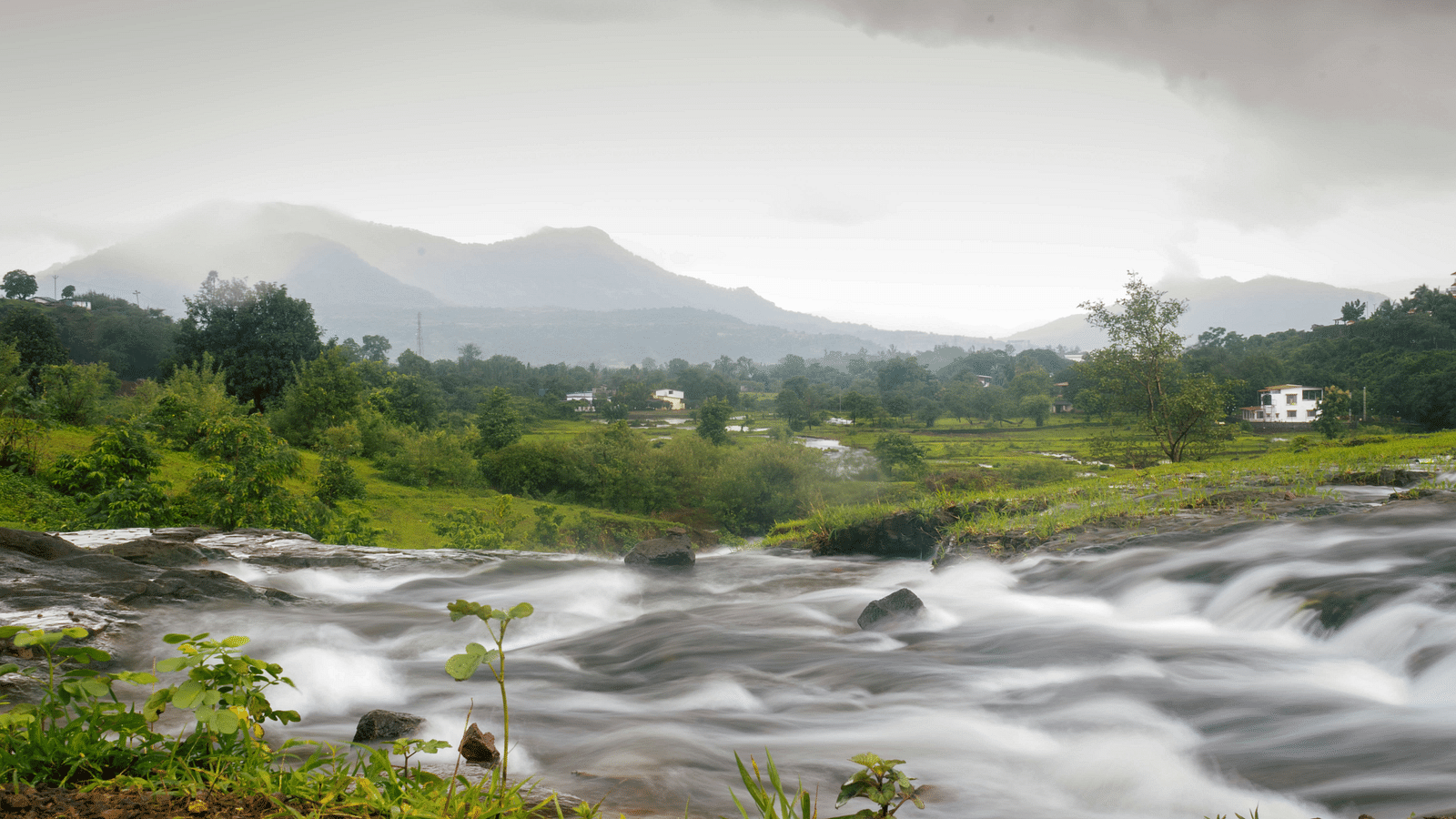 A river flowing in between green land with mountains in the background in Karjat