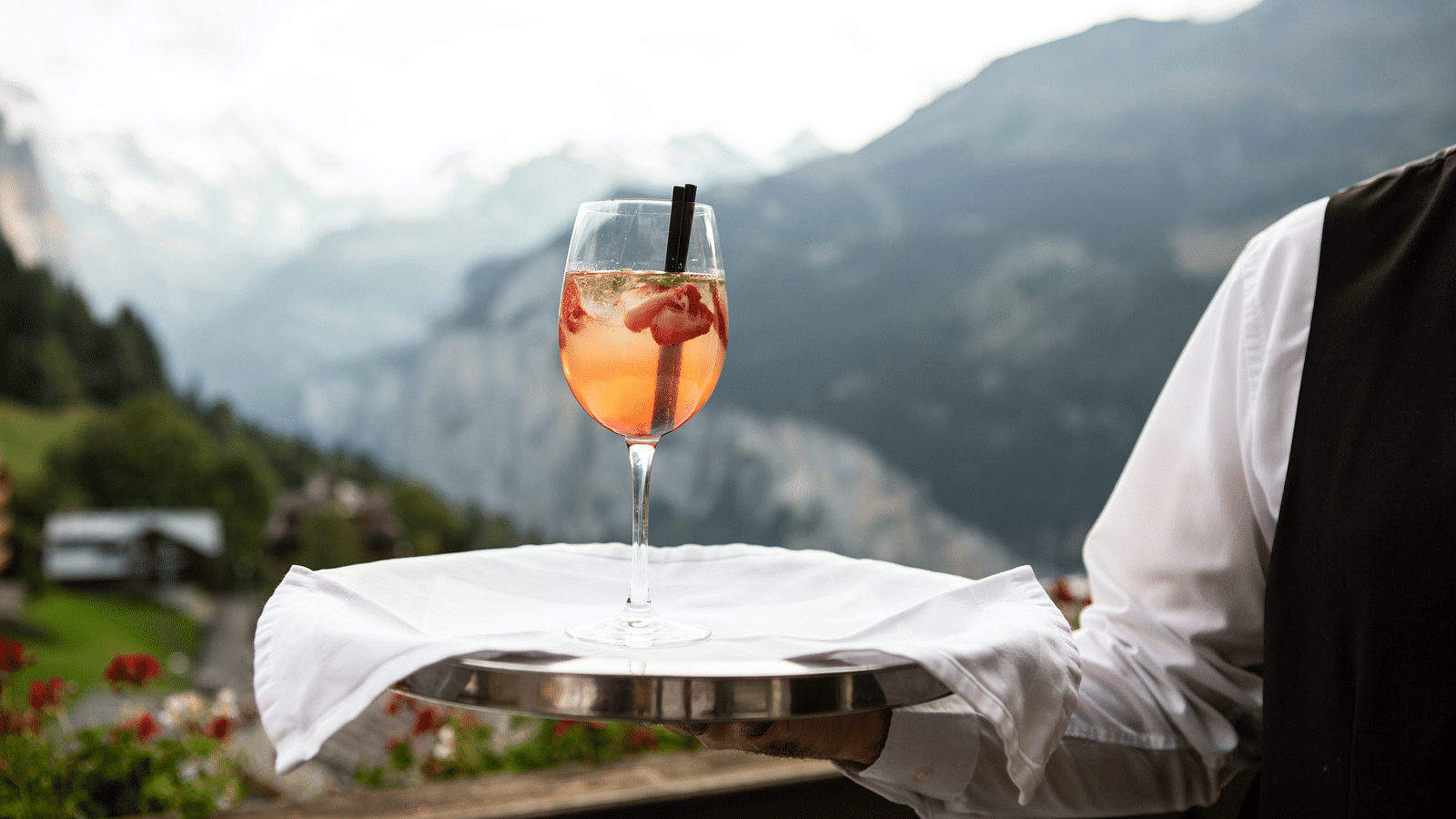 A waiter holding a tray with a mocktail with mountain ranges in the background 