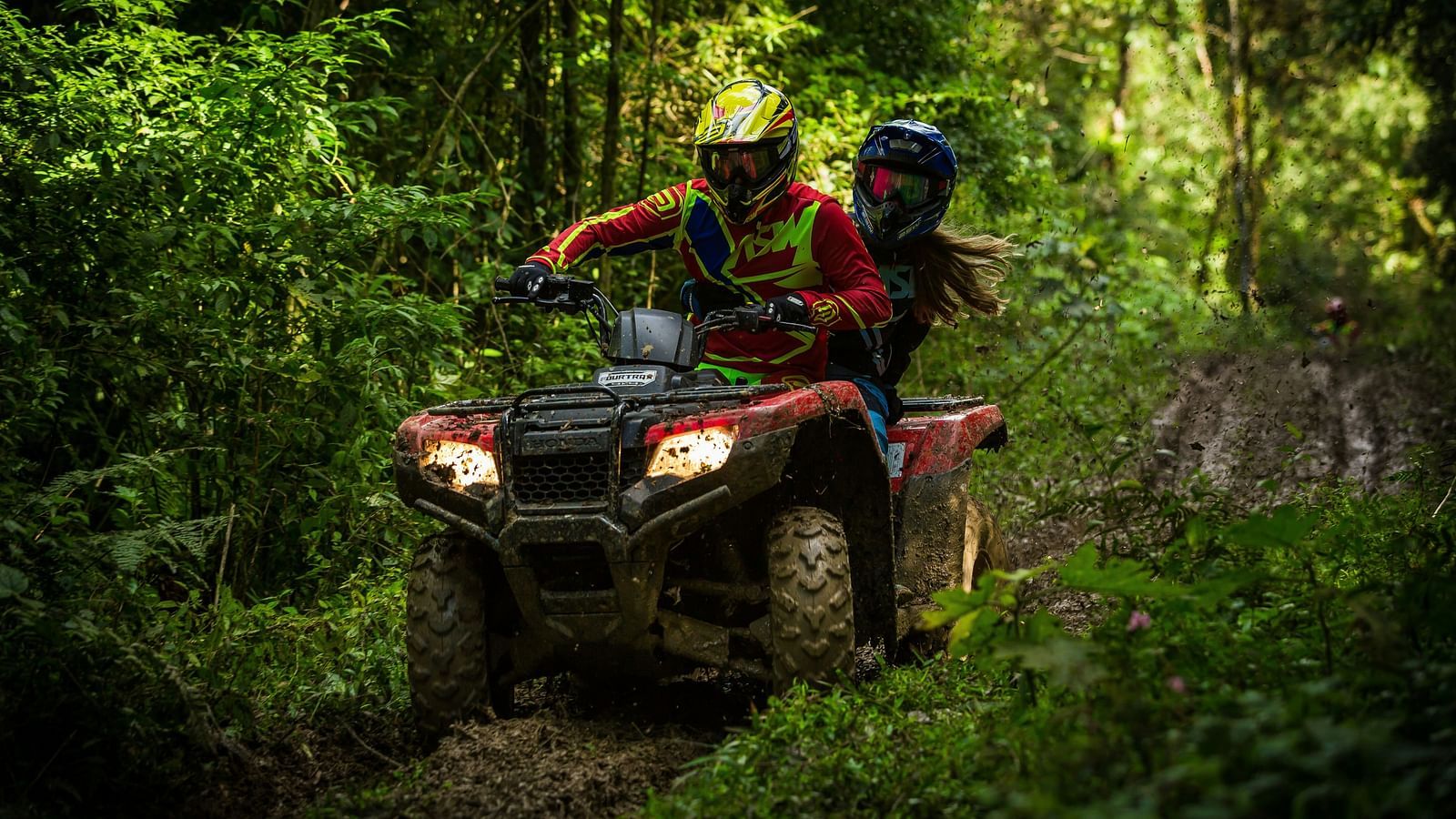 A couple enjoying an ATV bike ride through a muddy track surrounded by lush green trees