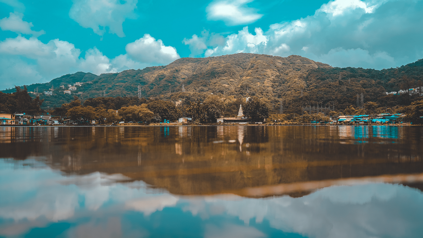 an image of a lake which reflects the white clouds over the blue sky and land in the background