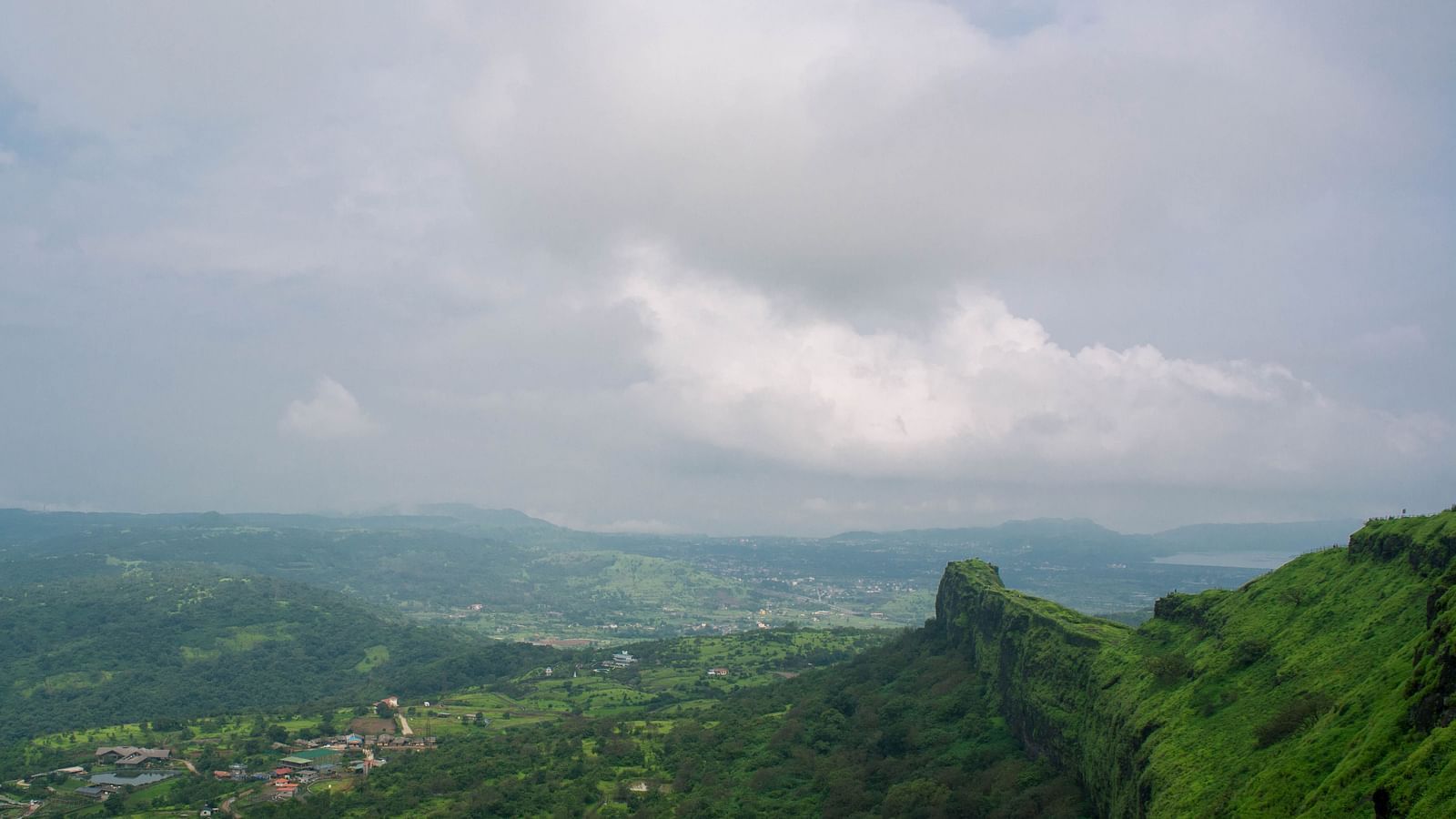an image of a view of a mountain cliff overlooking a town with white clouds above it
