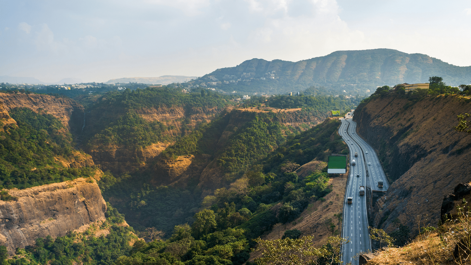 A highway cuts through a lush green landscape with a canyon and a waterfall in the background