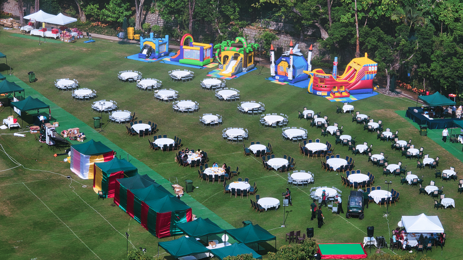 An aerial view of a lawn area with many tables set up and a children's area near the trees.
