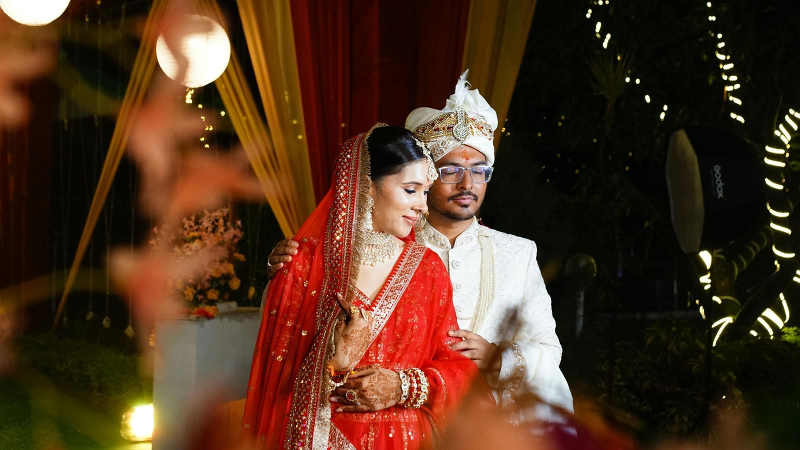 A bride and groom in traditional Indian wedding attire pose together.